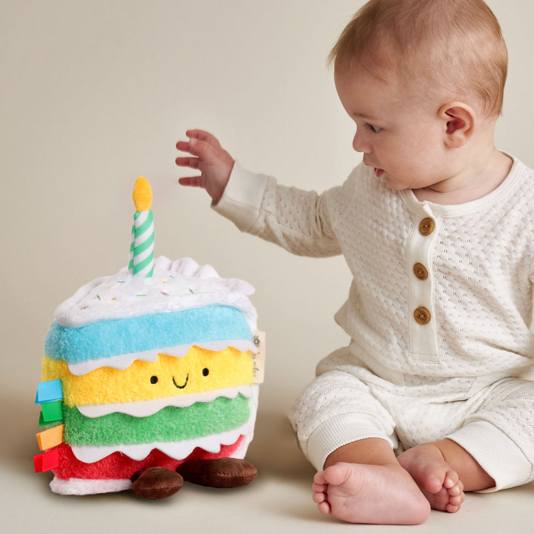 Baby interacting with a colorful plush cake toy with a candle